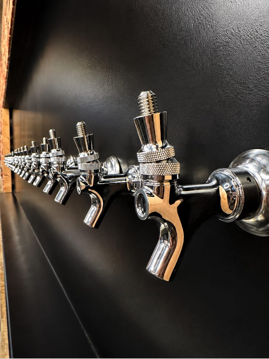 A long row of polished chrome beer faucets mounted along a matte black wall behind the bar.